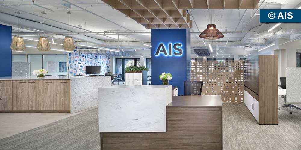 Brightly lit AIS Showroom featuring vignettes of modern office furniture and a large blue column in the middle with a backlit AIS sign. (Photo copyright: AIS)